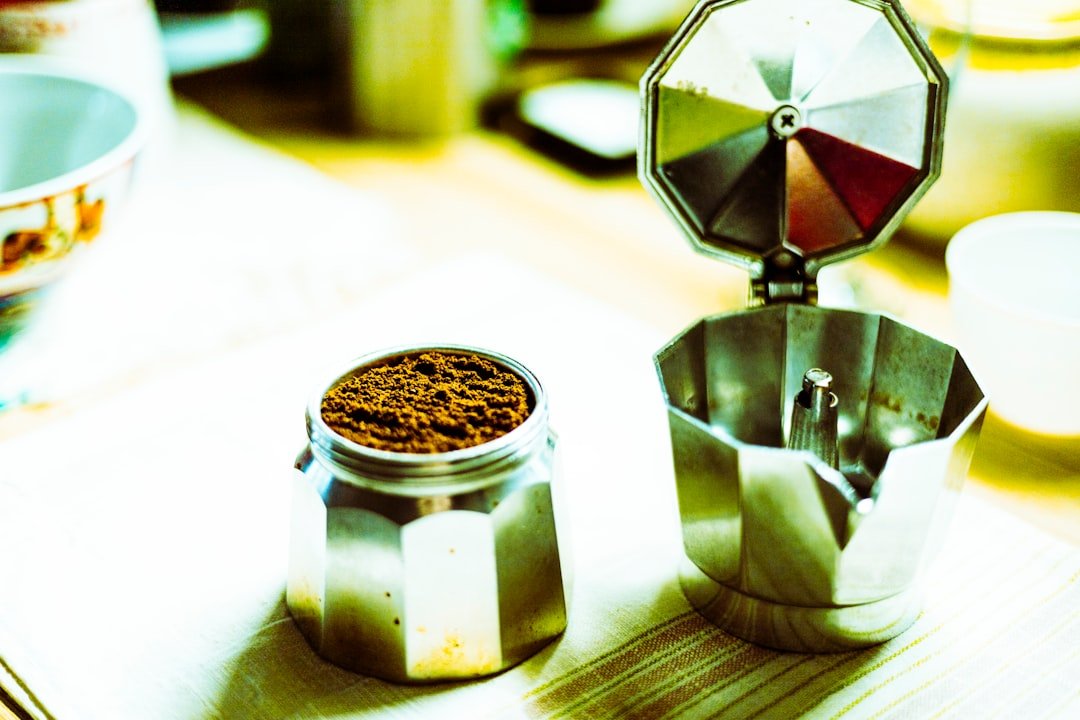A stovetop moka pot opened beside freshly measured coffee on a bright kitchen counter.