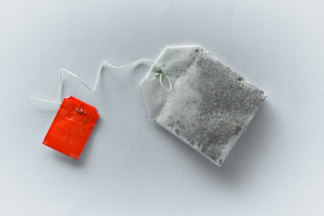 A single tea bag with a red tag on a light surface