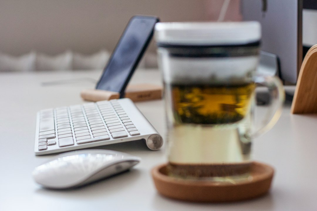 clear glass cup on round drink coaster beside Apple Magic Mouse and wireless keyboard